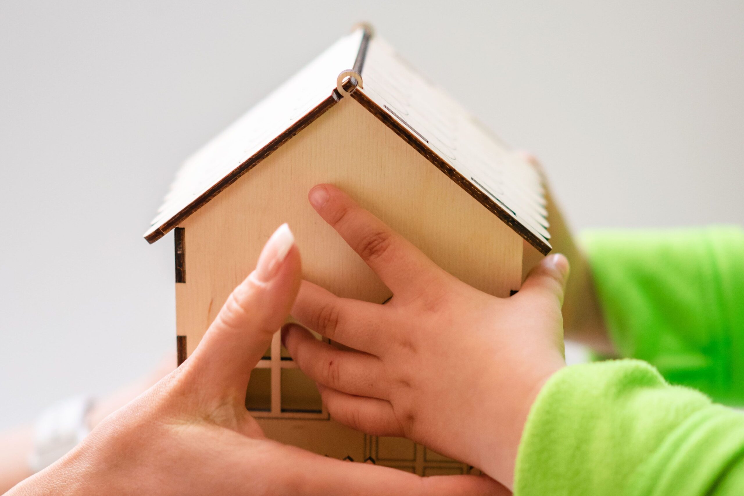 Close-up of mother and child holding a small wooden model house, symbolizing family and home.