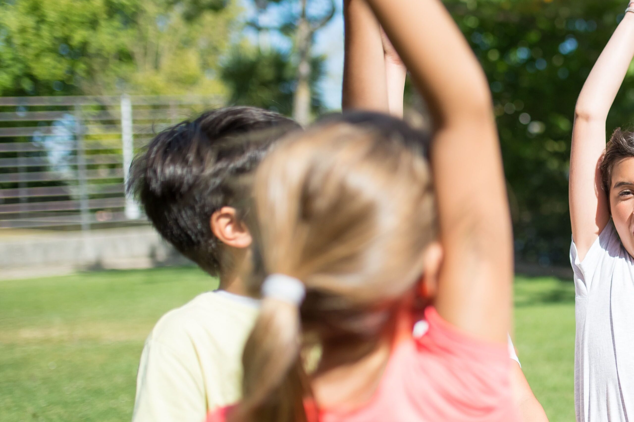 Group of children playing with raised arms in a sunny park, enjoying summer fun.